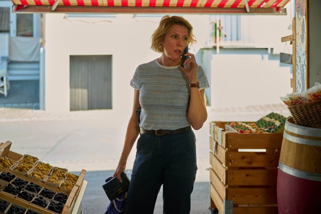 "Mordufer - Brennen soll sie": Doro Beitinger (Franziska Weisz) steht im Eingangsbereich eines Hofladens und telefoniert mit ihrem Smartphone, welches sie in ihrer linken Hand hält. In der rechten Hand hält sie einen Geldbeutel und eine Einkaufstasche.