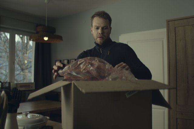 “Der Garmisch-Krimi - Wolfsmord“: Fabian Pongratz (Ben Münchow) steht in seiner Küche. Auf dem Tresen steht ein großes Paket, das er gerade öffnet. Schockiert blickt er auf den nicht sichtbaren Inhalt des Pakets und die aus dem Paket herausragende, blutverschmierte Plastiktüte.